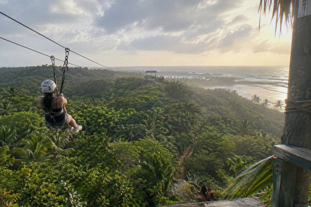 A rider in a helmet and harness gliding along a cable above tropical forest