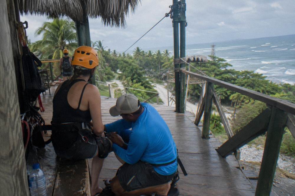 A guide fastening a harness strap on a seated guest at a jungle platform