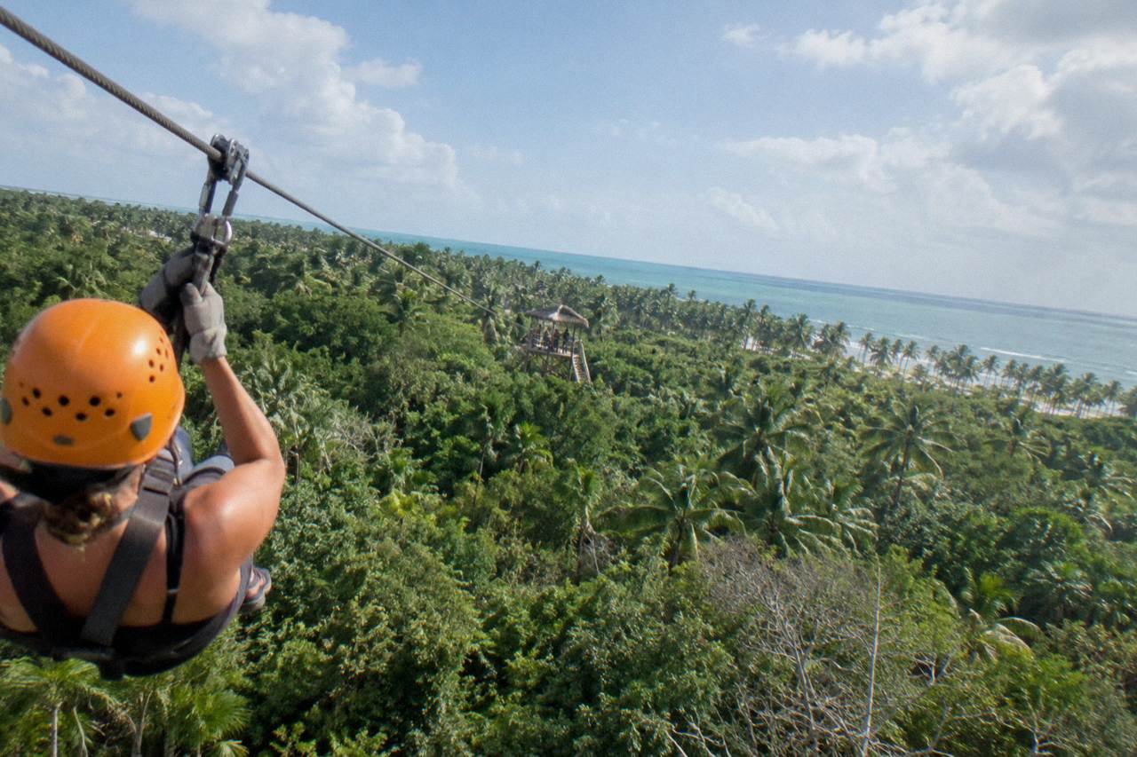 A zipline cable stretching over green jungle canopy toward a distant wooden platform