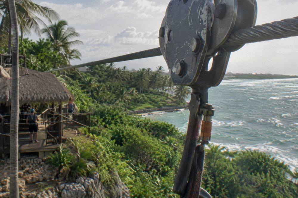 A zipline trolley and pulley wheel resting on a steel cable above tropical treetops