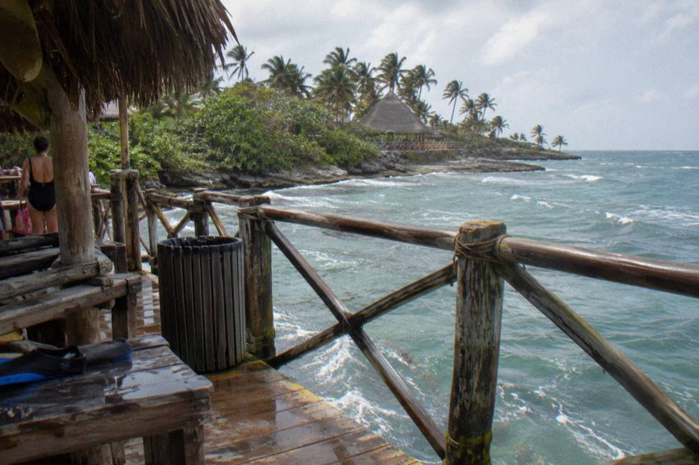 A padded zipline harness and helmet hanging on a wooden platform railing in jungle shade