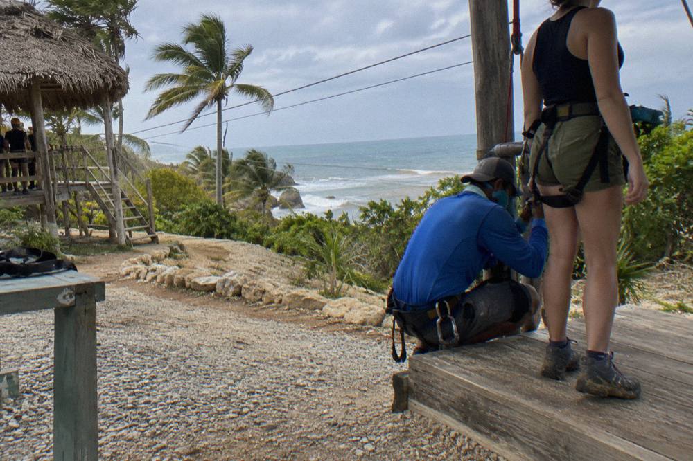 Guide tightening a zipline harness buckle on a wooden gear-up platform