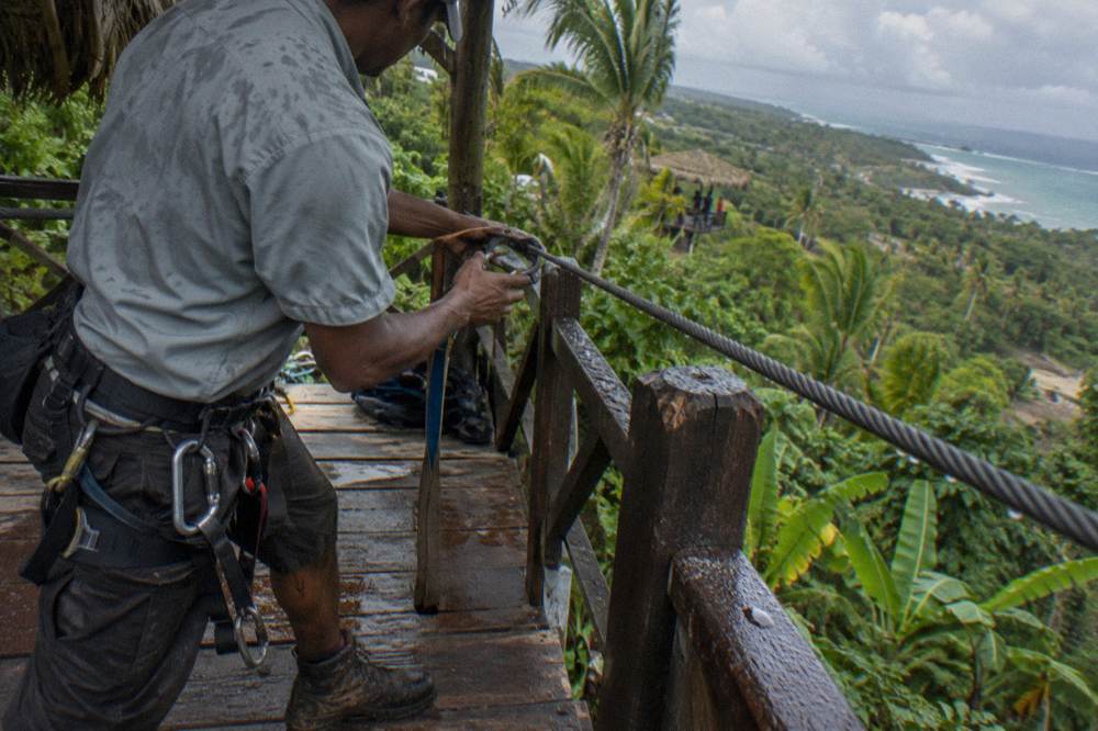 A guide attaching a harness carabiner to a zipline cable at a jungle platform