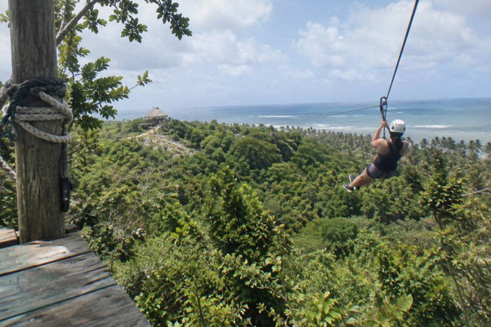 Traveler in a harness riding a long zipline above a green jungle valley