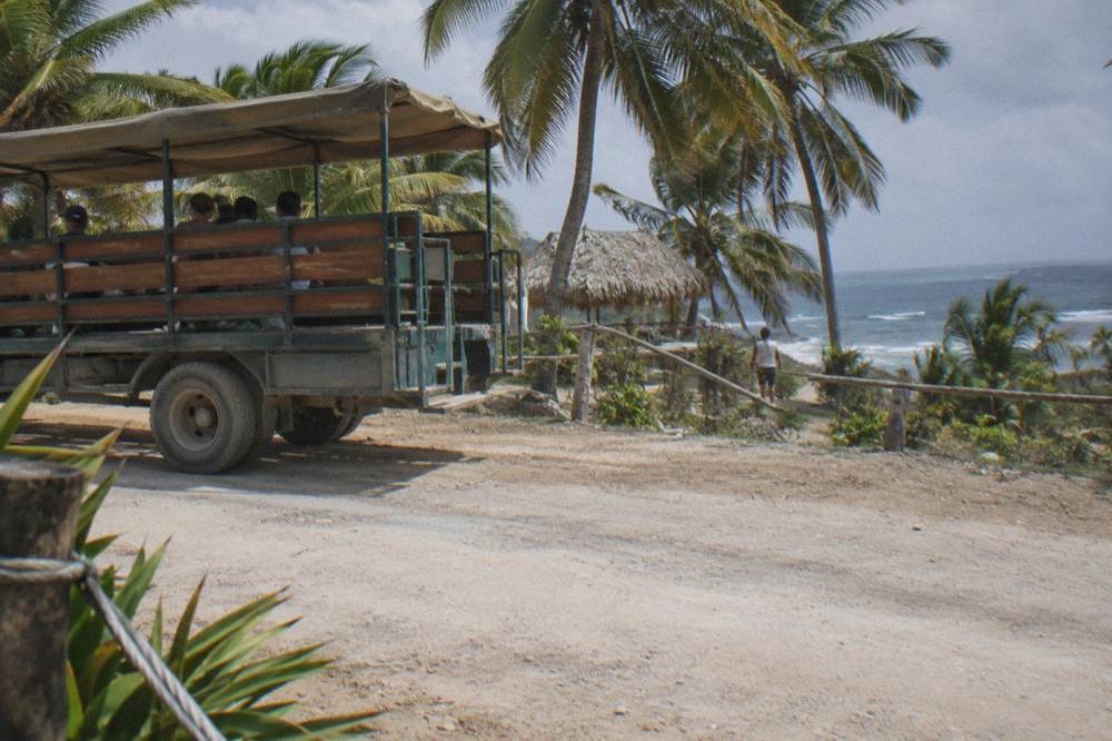 An open safari-style tour truck parked on a rural road beside palm trees