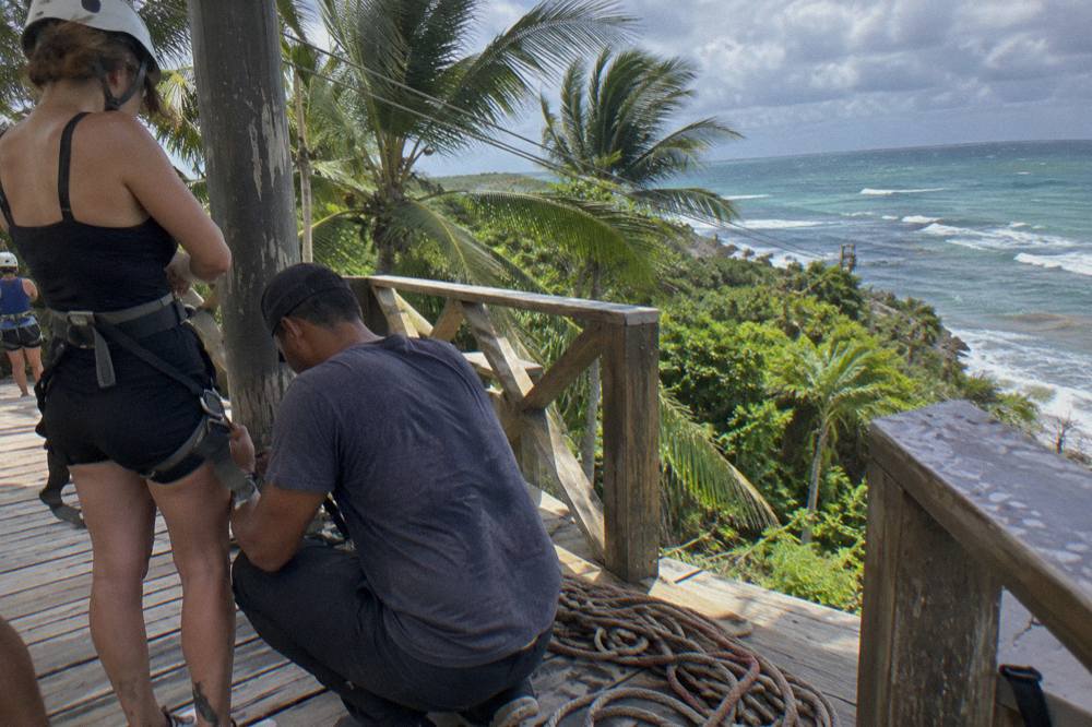 Guides fitting a safety harness and helmet on a zipline platform before a flight