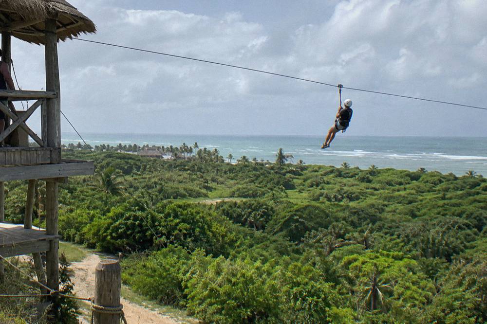 Person in helmet and harness riding a zipline above a green forest valley
