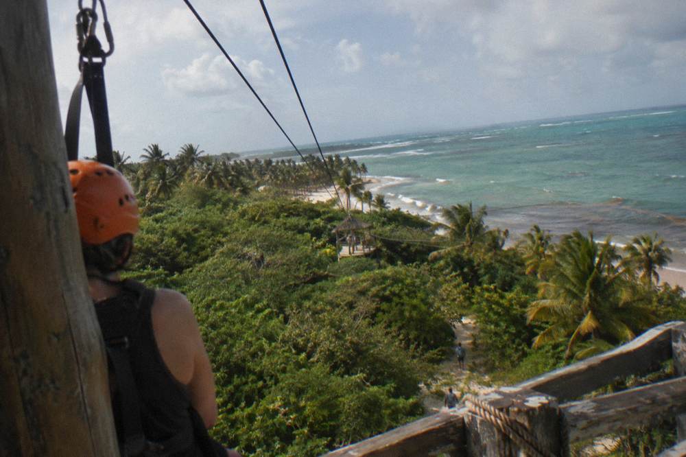 Person in helmet and harness standing on a wooden zipline platform above the forest