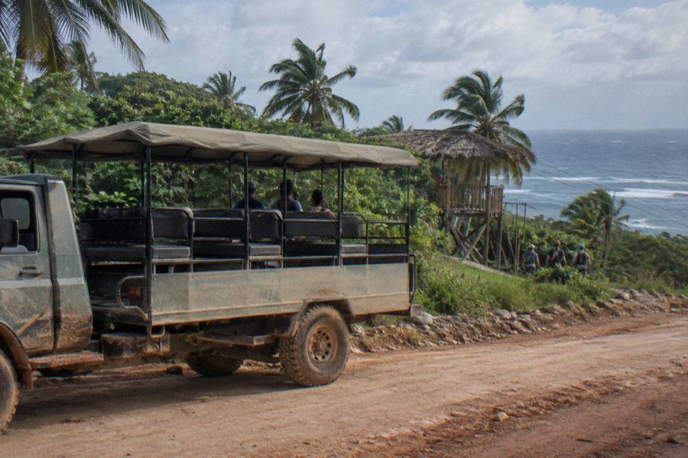 Shared safari-style truck parked on a dirt road beside jungle on the way to a zipline base