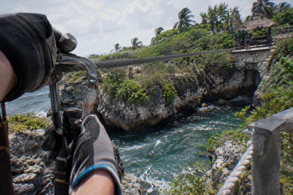 Guide clipping a carabiner onto a steel zipline cable above a forested valley