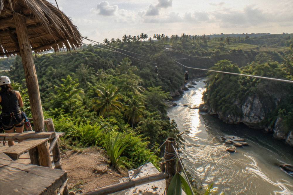 Two parallel zipline cables stretching far over a river gorge between forested ridges