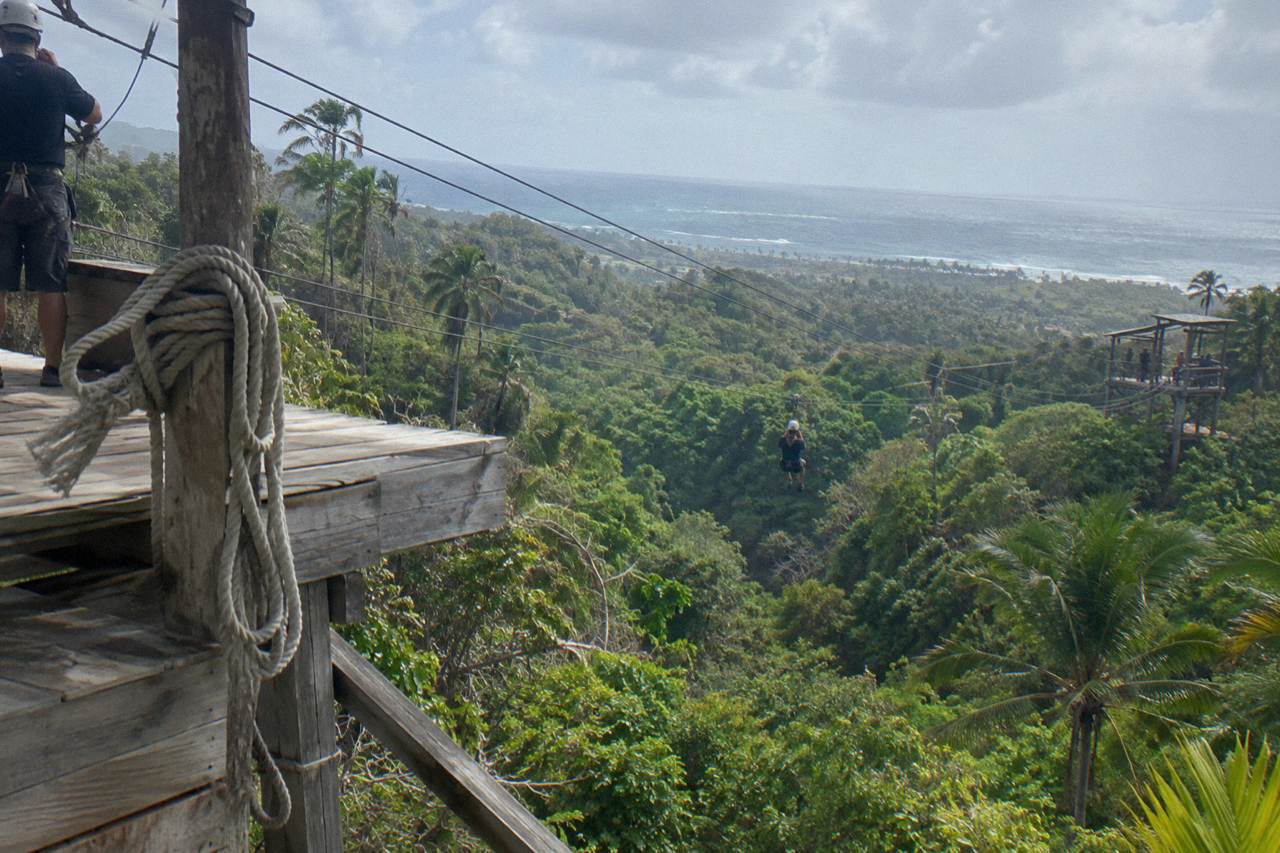 Zipline cables strung between wooden platforms above dense green jungle canopy in a mountain range