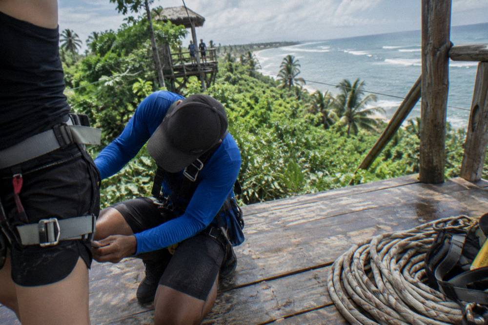 Guide tightening a harness strap on a guest prepared for a zipline run