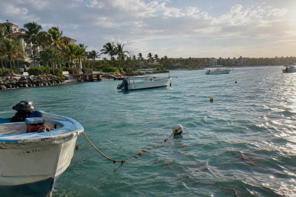 Calm turquoise bay with white sand, thatched shade umbrellas and moored small boats