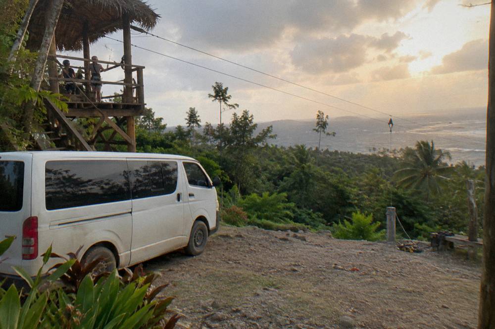 Private van parked beside a jungle canopy platform while a small group unloads gear