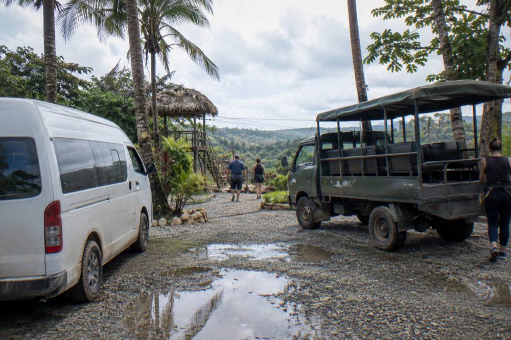 Tour van and safari truck side by side at a zipline base parking area in the hills
