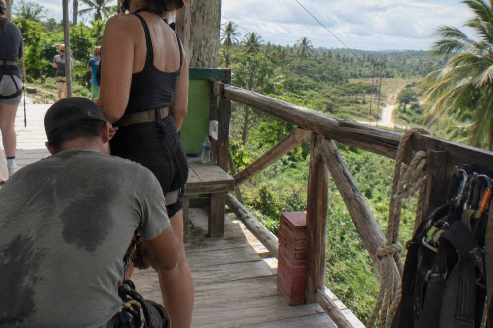 Guide checking a zipline harness buckle on a wooden launch platform in the jungle