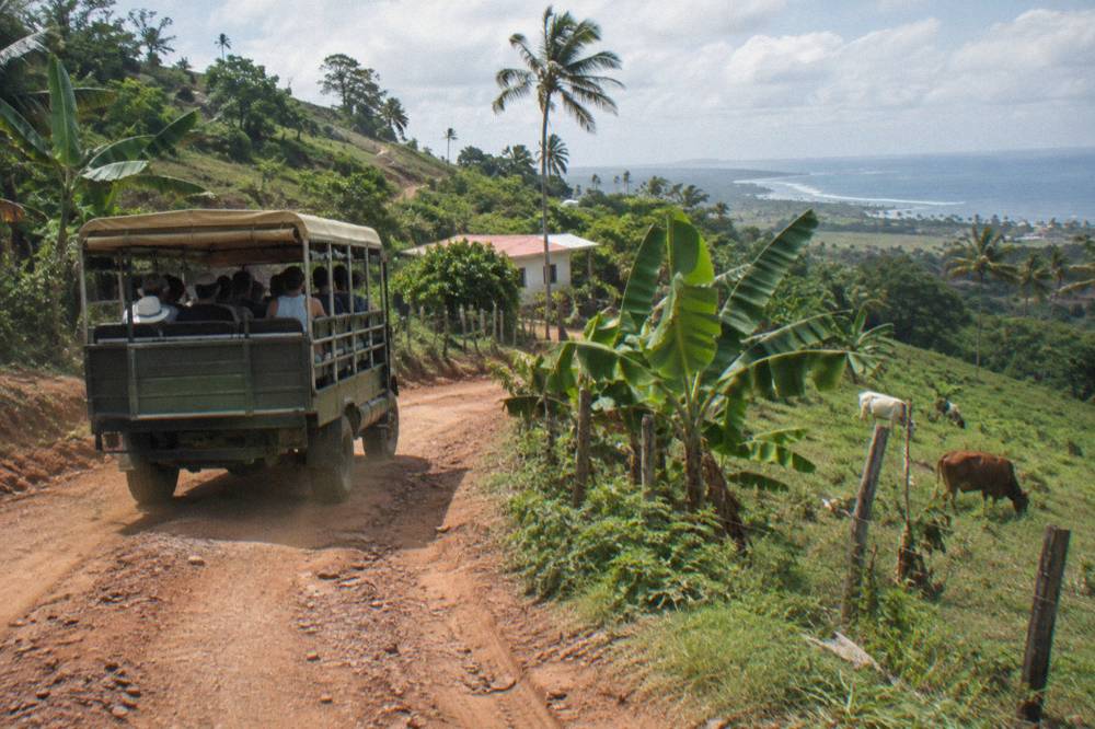 Shared open-sided safari truck driving on a dirt road through tropical hills