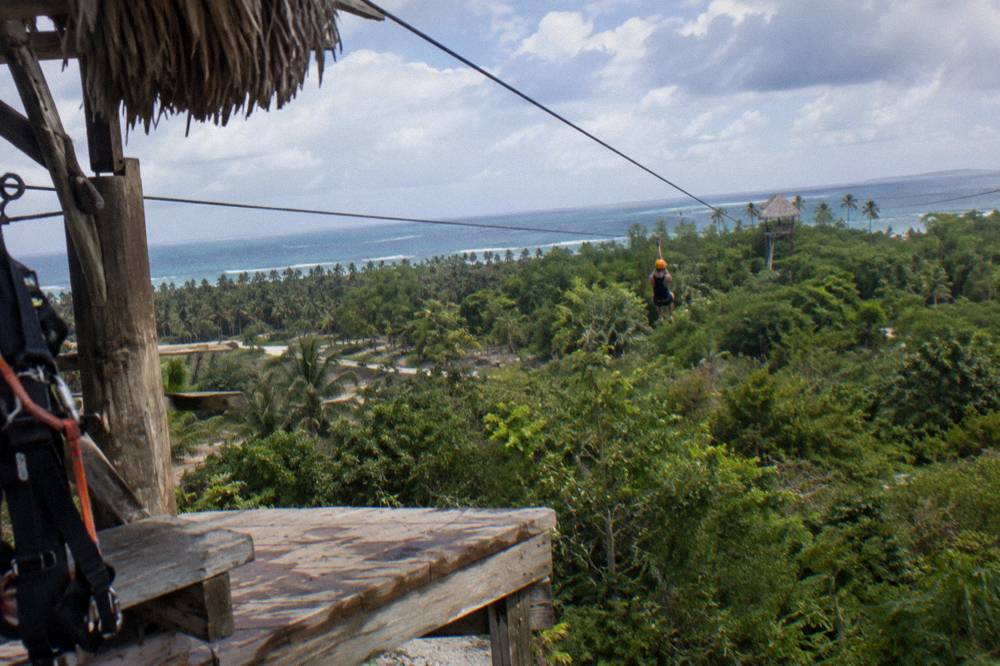 Wooden zipline platform overlooking a wide valley of tropical forest under scattered clouds