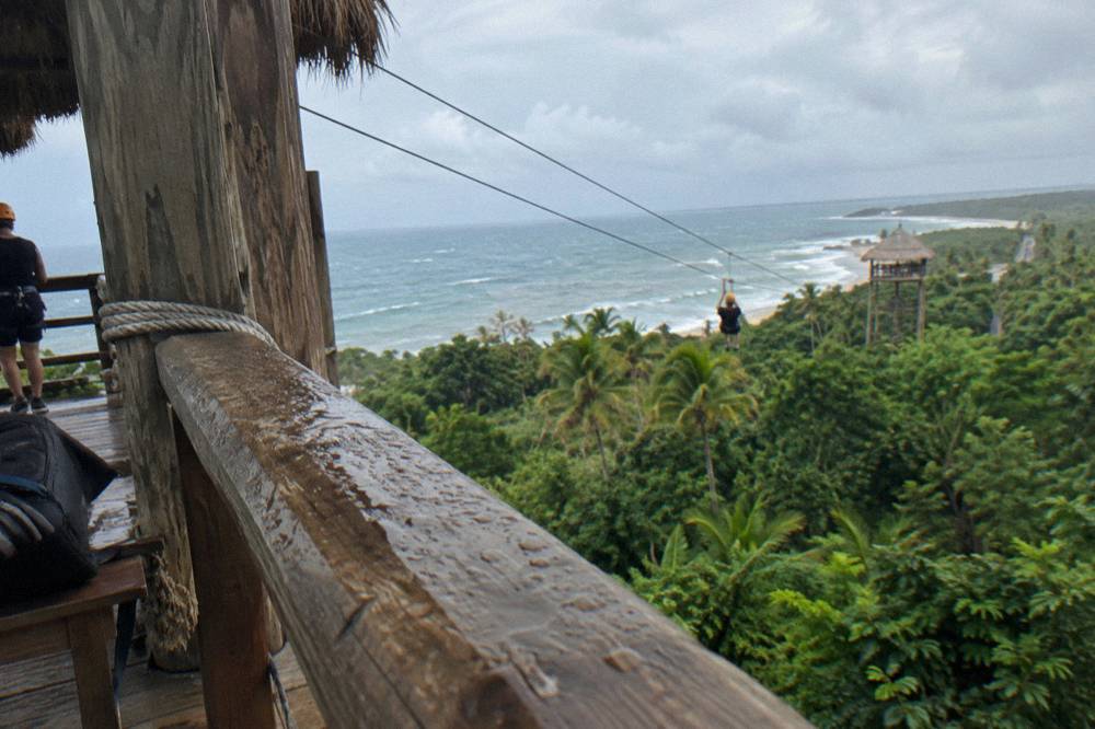 Zipline harness and helmet hanging on a wooden platform under an overcast jungle sky