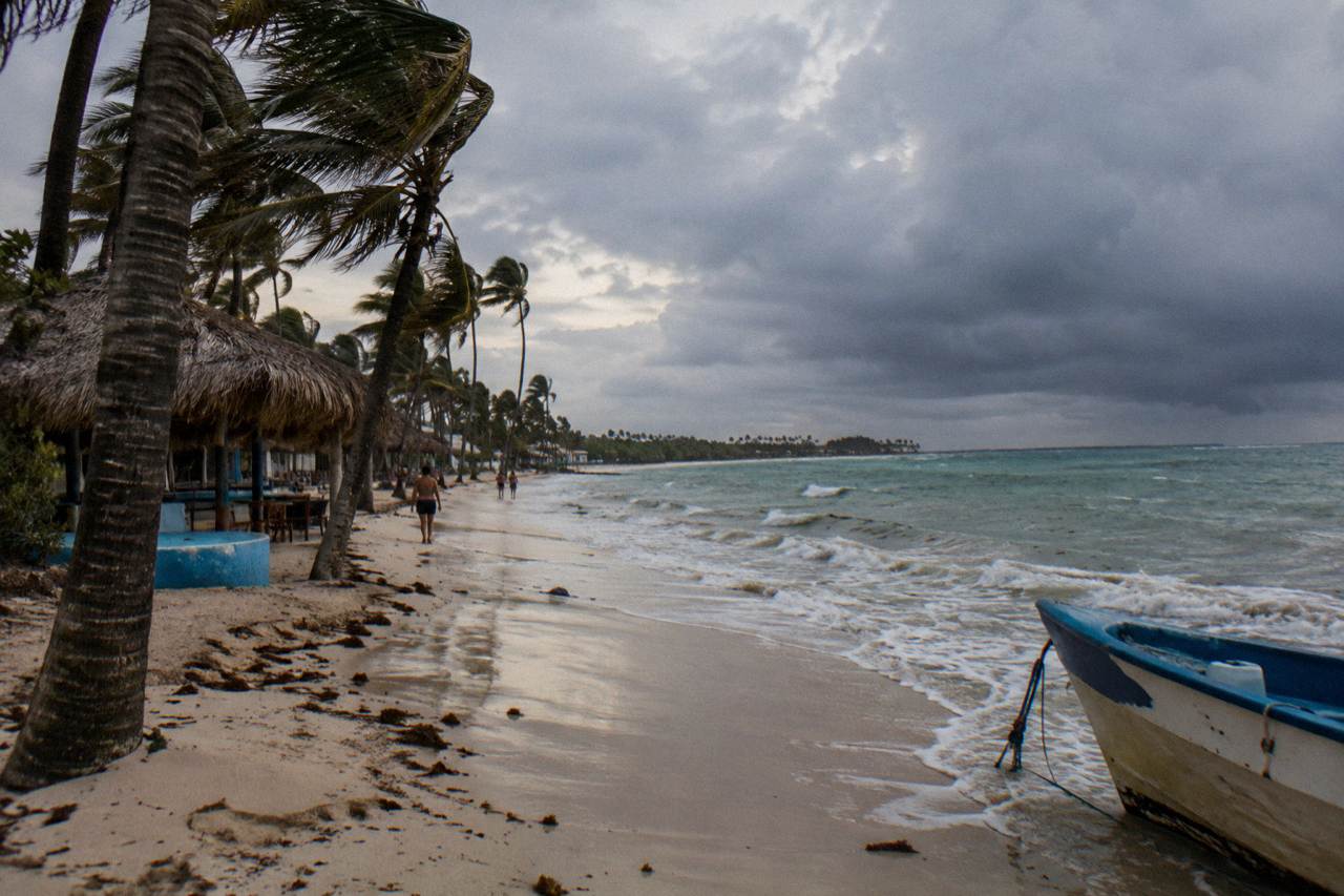 Palm trees bending under gray storm clouds over a calm Caribbean beach