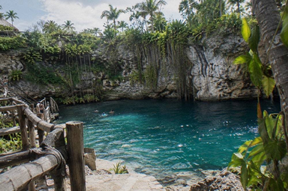 Turquoise freshwater cenote ringed by limestone cliffs under palm trees