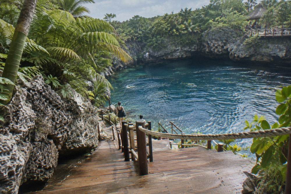 Wooden boardwalk descending through ferns and rock toward a blue waterhole