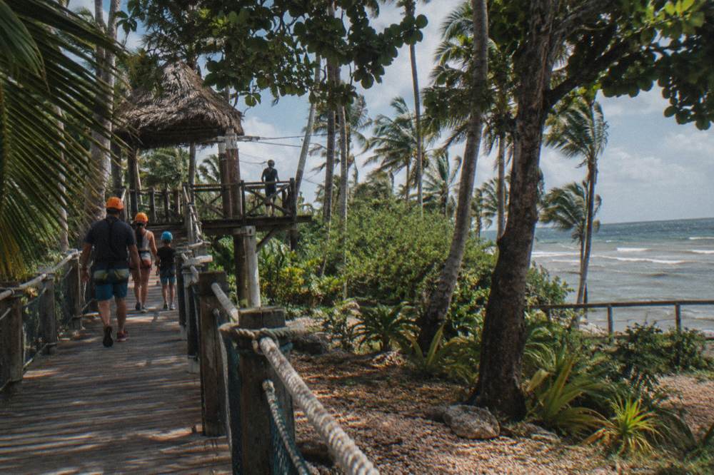 Family walking along a raised wooden walkway between zipline platforms in tropical woodland