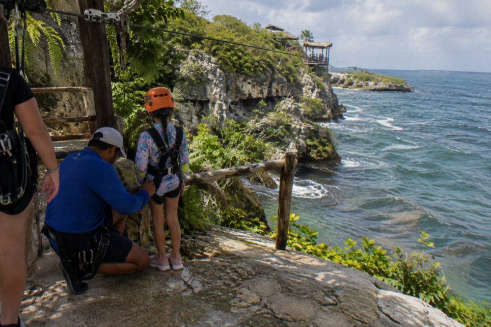 Guide checking a harness strap on a young zipline rider at a jungle platform