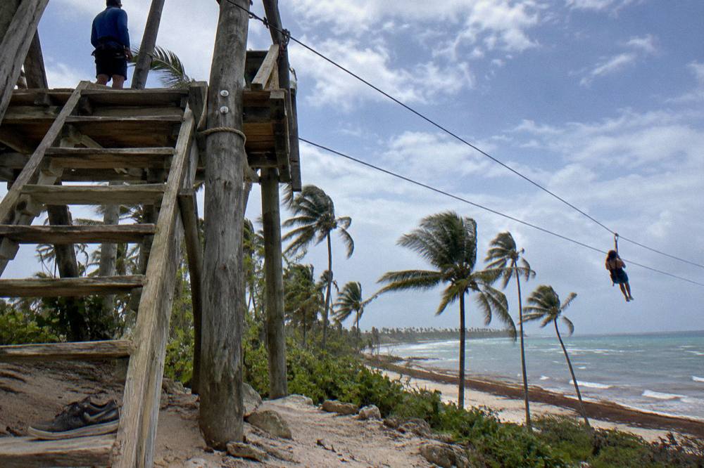 Wooden zipline platform and cables above tropical treetops under a partly cloudy sky