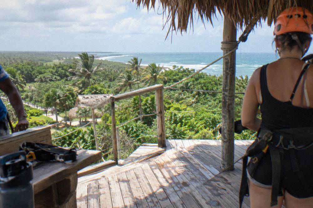Helmeted rider on a zipline platform above dense tropical forest