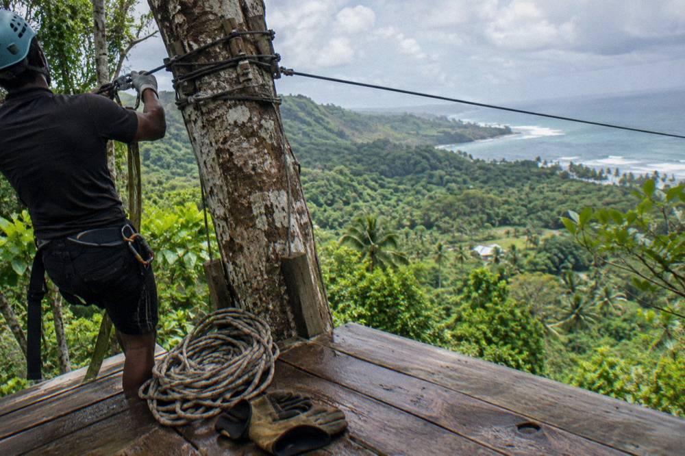 A wooden zipline platform in the jungle with a guide clipping a harness cable.