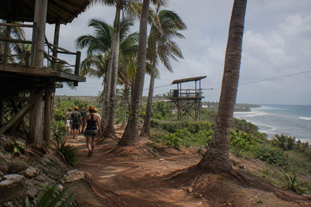 A group of helmeted zipline riders walking a trail between jungle platforms.