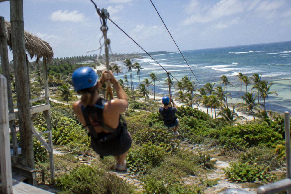 Two zipline riders in helmets and harnesses preparing on a wooden platform