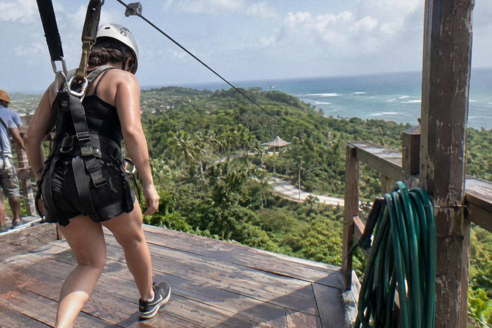 A rider in a full harness stepping off a wooden launch platform onto a zipline cable