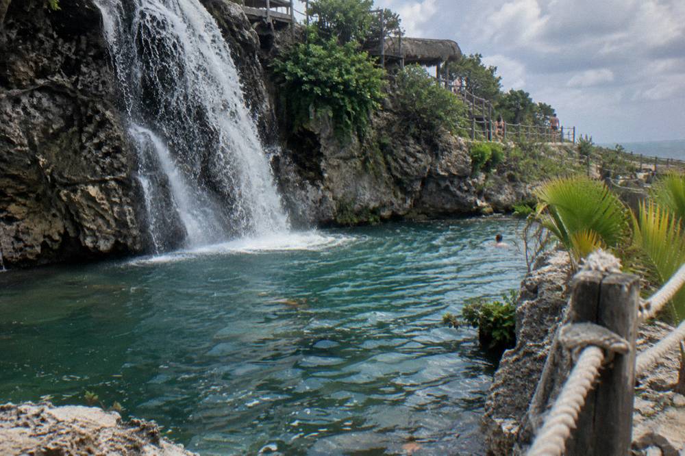 A waterfall pool at an adventure park with water cascading over dark rock into a clear pool