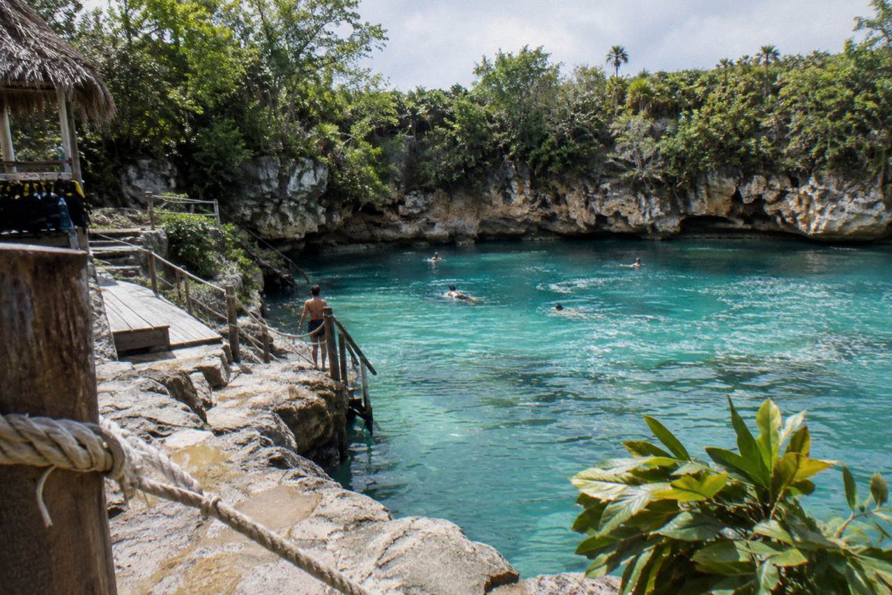 A turquoise cenote pool ringed by rock walls and jungle vegetation